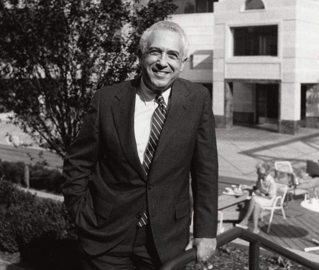 Black and white photo of Leonard Laster, M.D., a smiling white man in a suit, standing at The Vollum Institute at OHSU in Portland, Oregon.