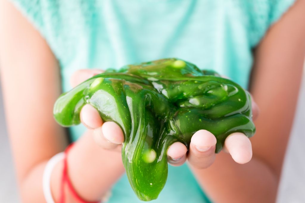 Closeup shot of a child's hands holding homemade, olive green slime in their bare hands.