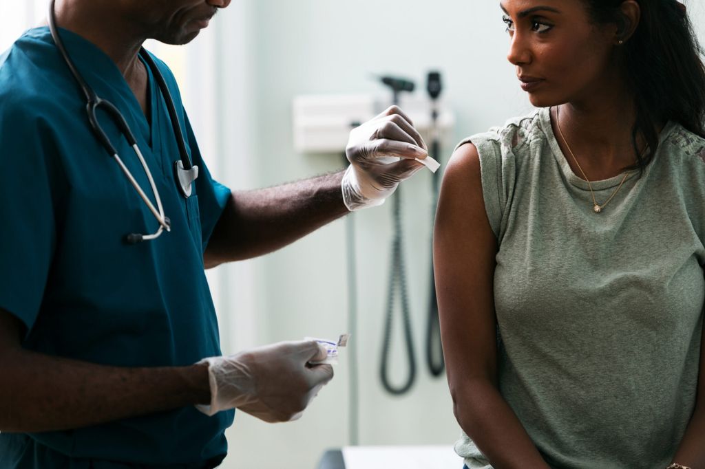 Exam: a black doctor swabs a black woman's shoulder with an alcohol pad.