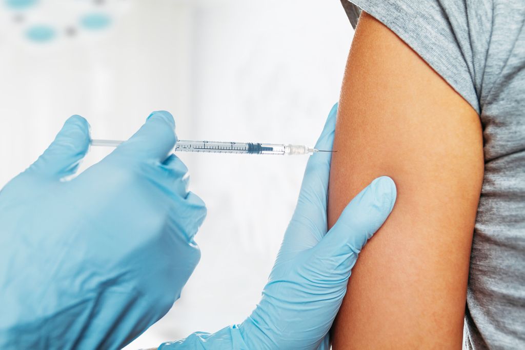 A health care professional gives an adult an injection in their shoulder; close-in image, no faces shown.