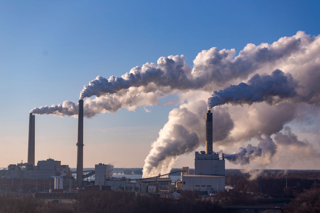 three industrial smokestacks pour smoke into the sky, which is blown by the wind