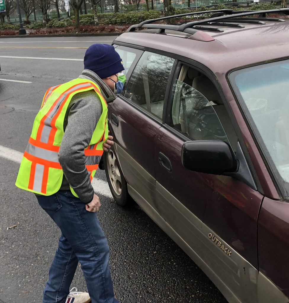 OHSU leader in yellow safety vest, mask and stocking cap directs traffic outside the Oregon Convention Center parking garage-turned vaccine clinic.