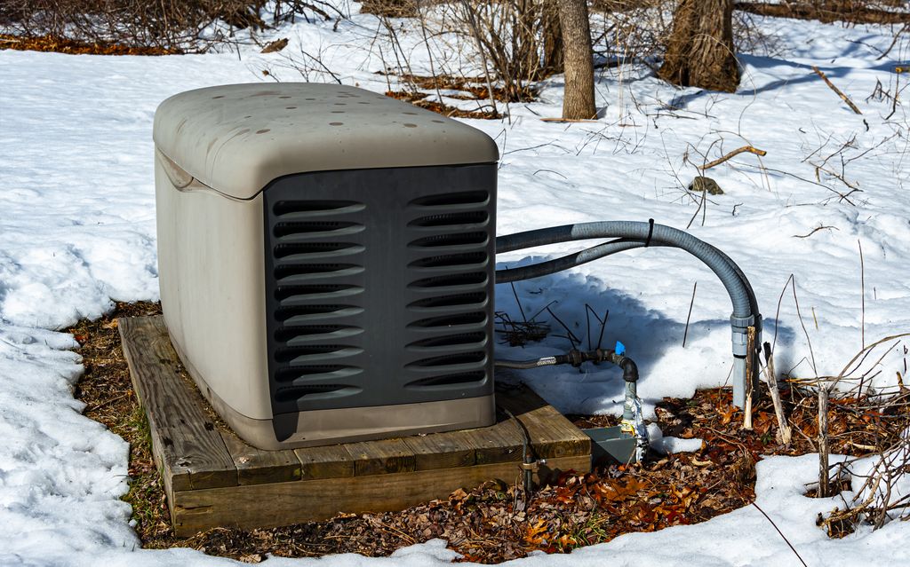 Residential generator outdoors in the snow, atop a wooden platform