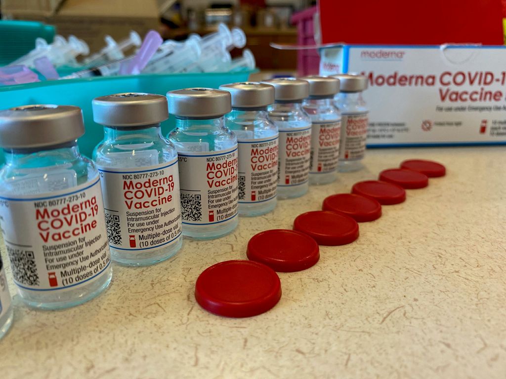 a row of vials of Moderna COVID-19 vaccine, with their red caps removed and placed beside the vials