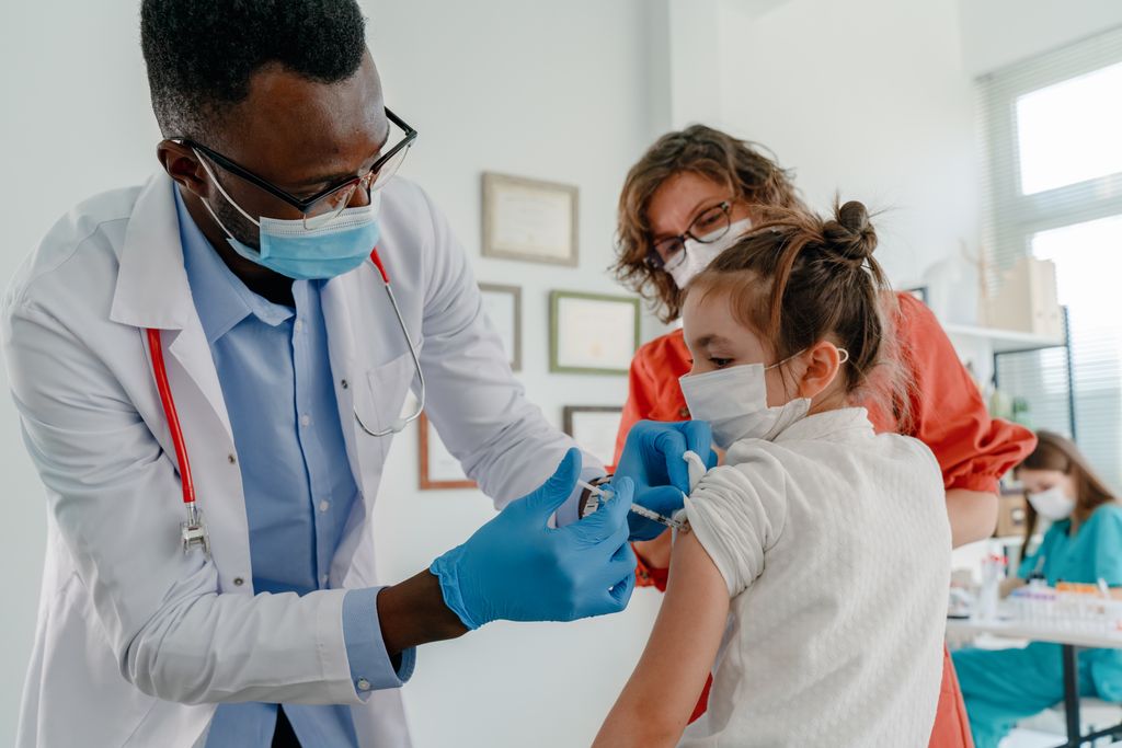 A girl gets a vaccination from her doctor while her mother looks on. (Getty Images)