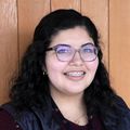 Gisela Ayala, a woman smiling wearing glasses, she has long dark hair.
