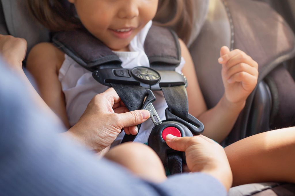 A toddler sitting in the child car seat with the mother helping to buckle and fasten seat beat properly to stay safe while driving. Learn more car safety tips during National Injury Prevention Day. (Getty Images)