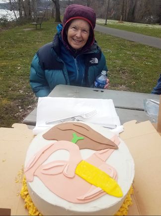 Anne Matsen, a woman in a coat and beanie, smiling next to a cake with a pancreas design on the top of it.