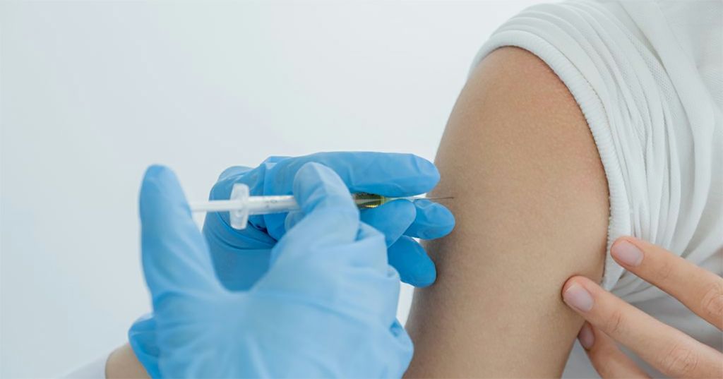 A person holding their arm while a medical professional injects them with  vaccine.