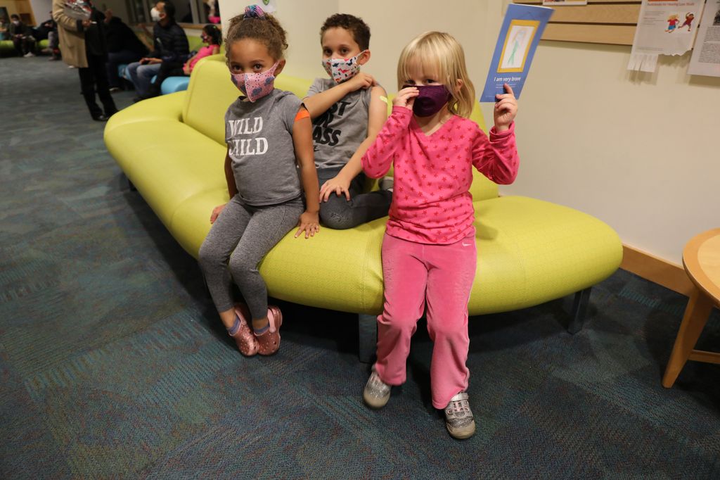 Three children sitting on a chair in the Doernbecher lobby after getting their COVID-19 vaccine.