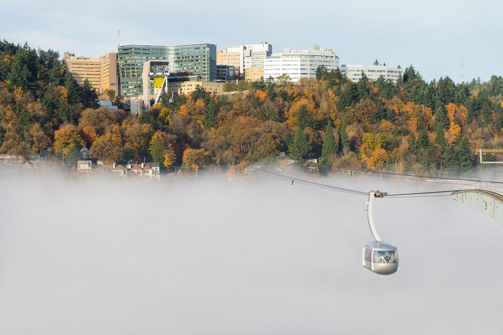 The OHSu sky tram glides across Portland on a foggy day with OHSU on Marquam Hill in the background.