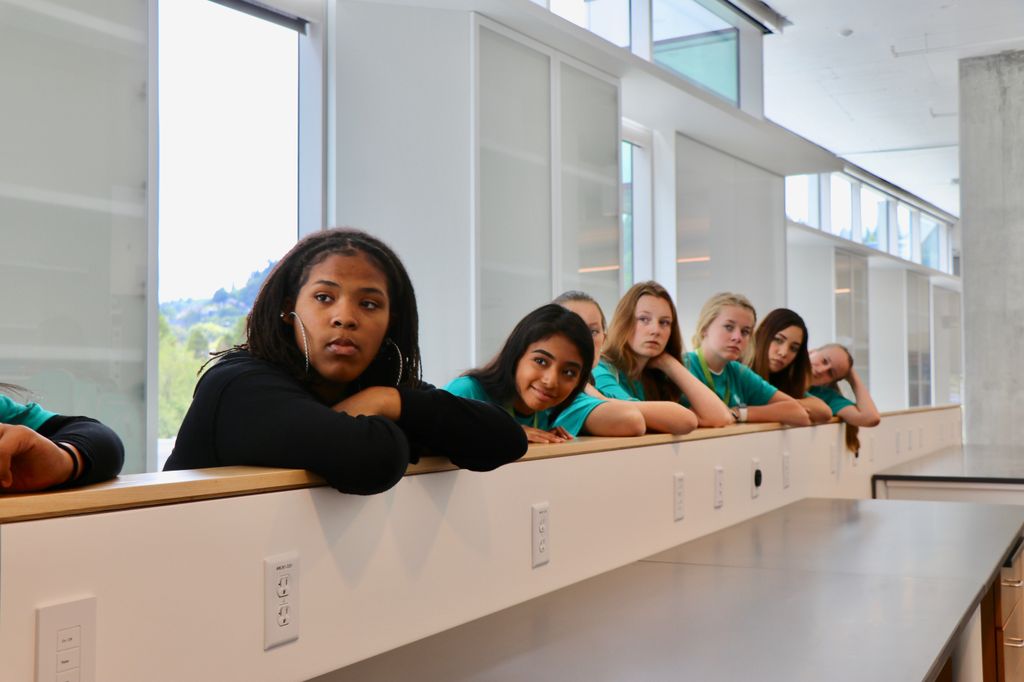 A row of young adults lean on a countertop and look in the same direction