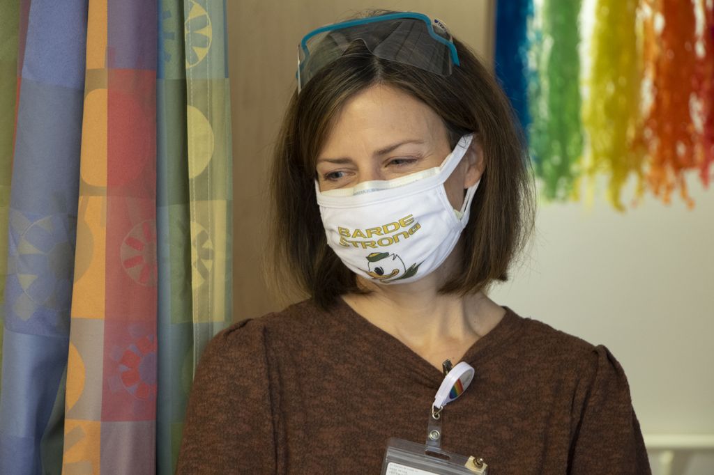 Woman with safety glasses propped atop her head smiles behind a face mask that reads “Barde Strong.”