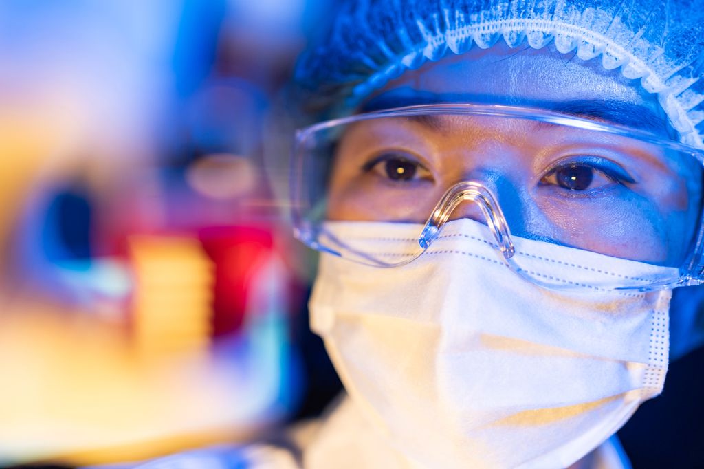 Close-up shot of face of female scientist working on virus vaccines (face in focus, foreground blurred)
