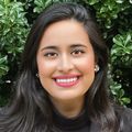 close-in headshot of Lubna Kahn, a smiling woman in red lipstick with black hair