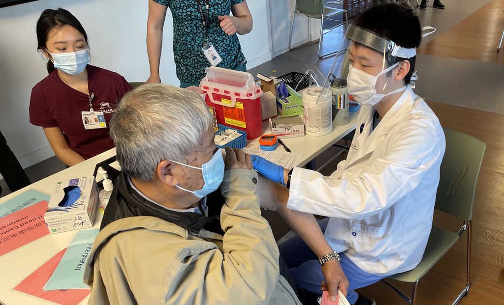 Asian Health & Service Center vaccinations - an elderly man gets a shot from a young health care worker.