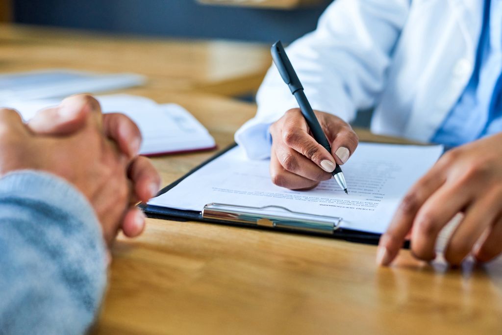 Closeup shot of a doctor's hands writing notes on a pad during a consultation with a patient