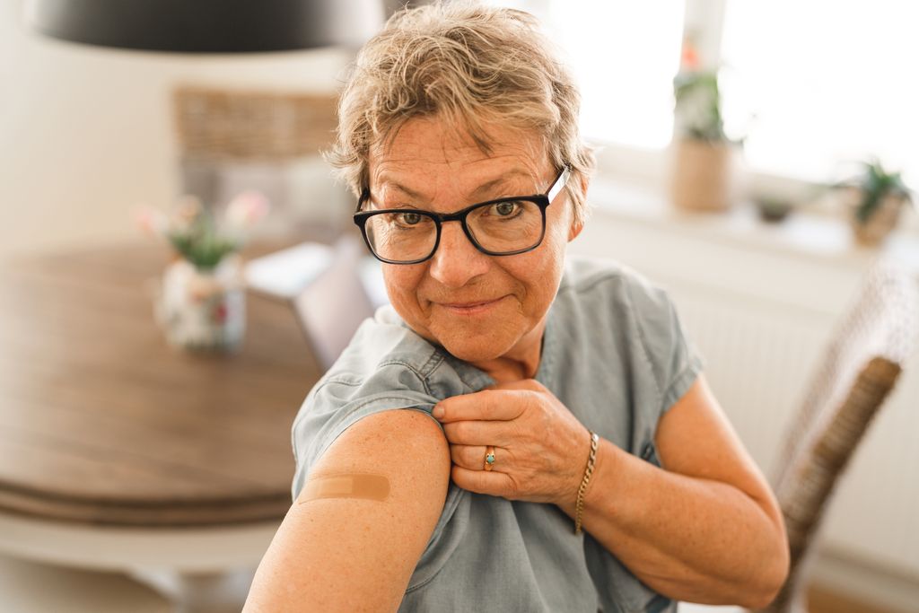 A senior woman that has received her COVID-19 vaccine. She is pulling up her sleeve to show the bandage.