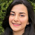 Close-in headshot of Neda Kazerouni, a smiling adult with long, brown hair, standing in front of greenery