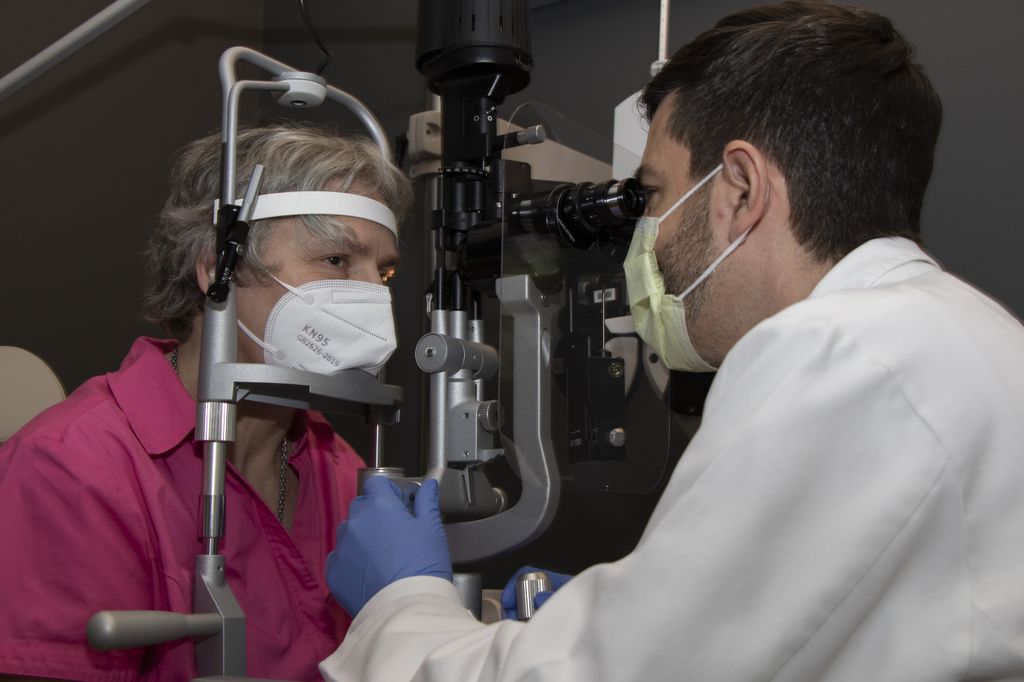 A man wearing a white coat looks at a woman’s eye through optical equipment.
