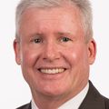 A suit-clad white man with grey hair smiles