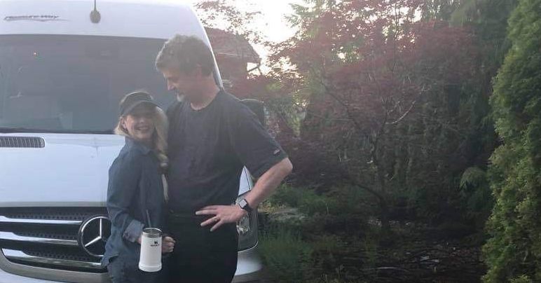 Kevin and Amanda Lyle, an adult male and female, stand outdoors smiling in front of a Mercedes Sprinter van
