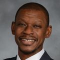 Portrait of Lishomwa Ndhlovu, M.D., Ph.D., a smiling Black man in a suit