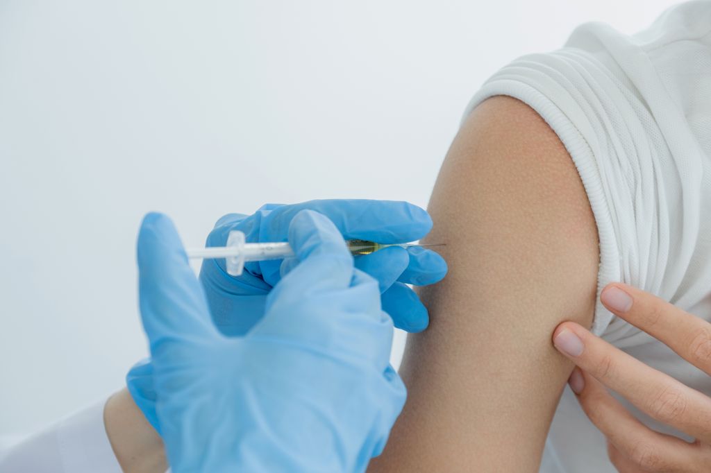 Person administering a COVID-19 vaccine into a patient arm.