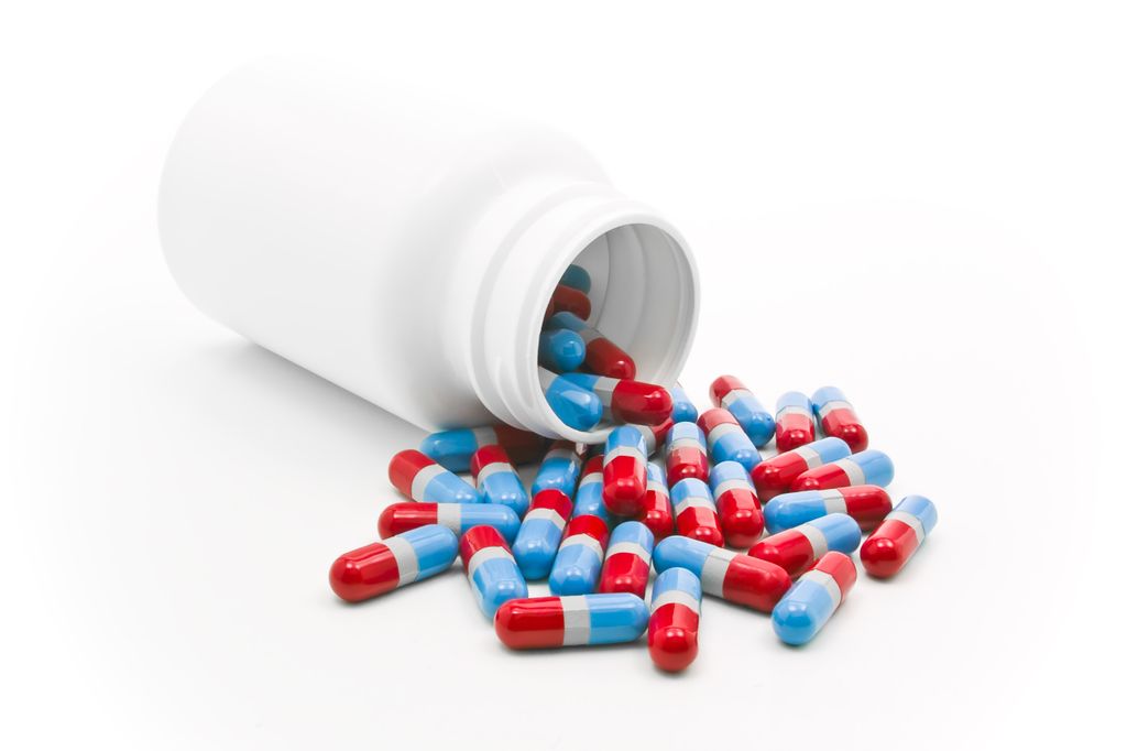 Blue and red pain killer capsules poured from a bottle. Isolated on white.