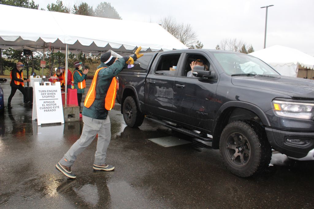 A volunteer in an orange safety vest rings a bell as a black truck leaves the premises with newly-vaccinated occupants.