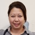 Portrait of Thao Ann Le, B.S., QMHA, a smiling Asian woman with dark hair wearing a brown top and black vest; a statue of an Eastern deity stands on the glass case she is leaning on.