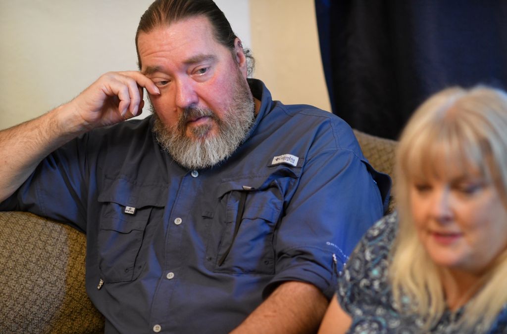A man wipes a tear from his cheek as a woman to his side looks on.