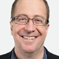 Close-in head shot of Eric Dishman, a smiling adult Caucasian man in glasses.