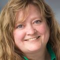 Portrait of Robin Gantt, a smiling Caucasian woman with long wavy hair and bangs.