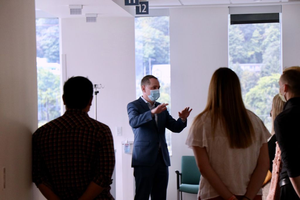 A man in a suit and surgical mask addresses a crowd of four standing people.