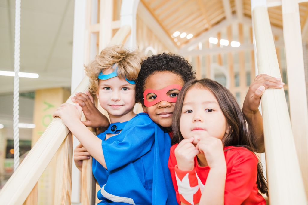 Intercultural little friends in costumes sitting on staircase in front of camera while playing together in children room