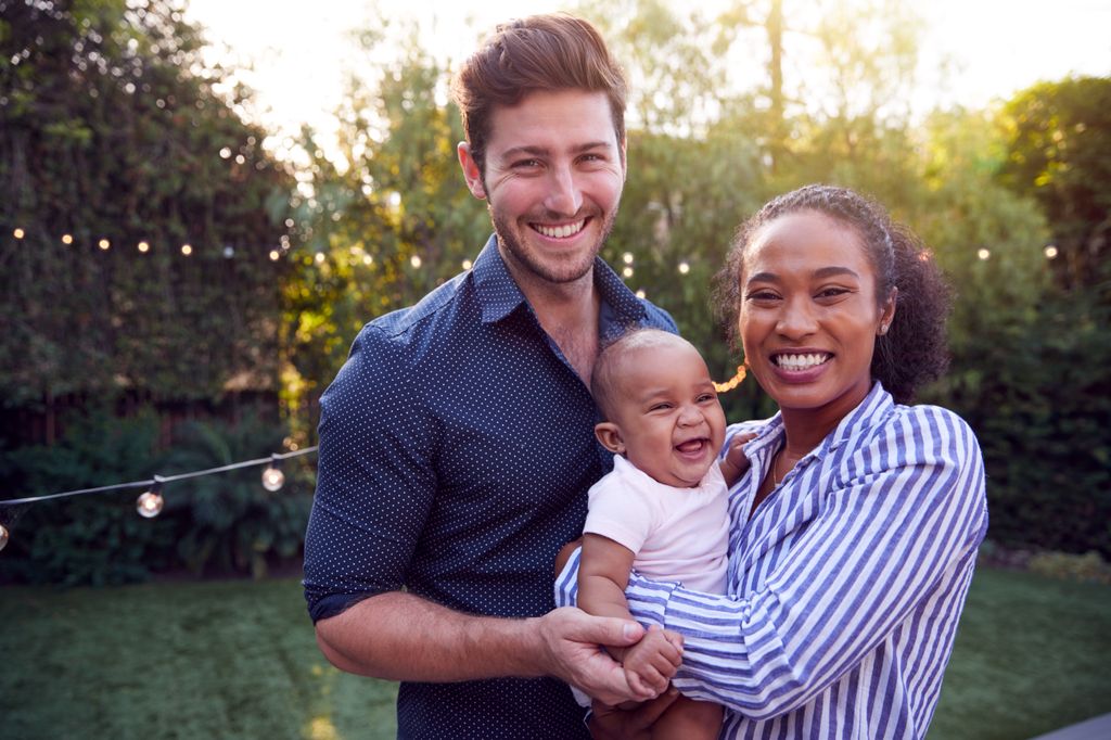 A man and woman hold a baby in a backyard, smiling.