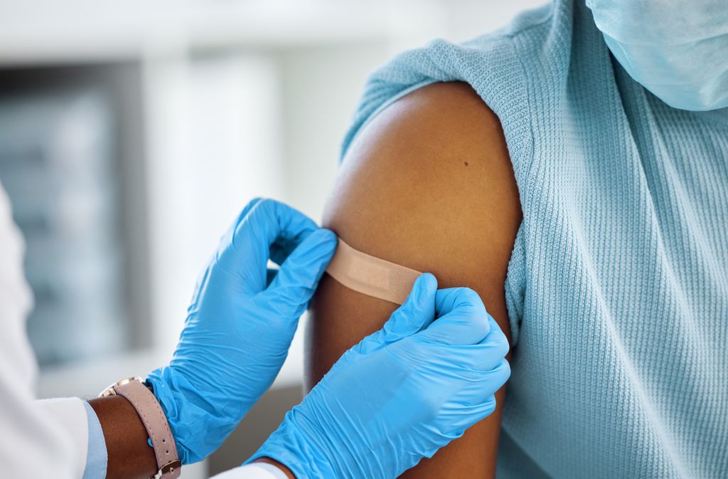 Image shows a person of female birth gender getting a vaccination in a healthcare setting.