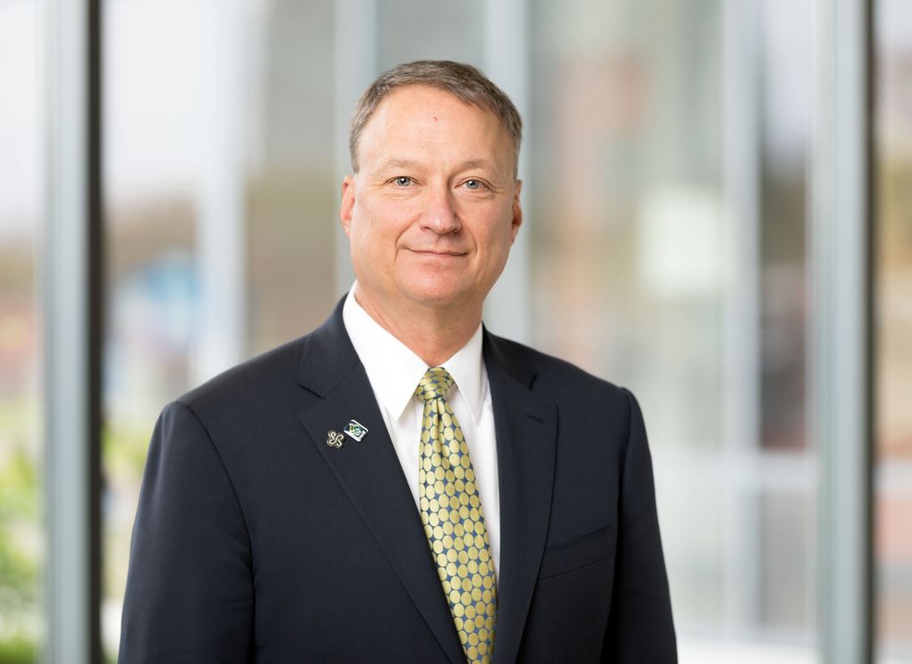 David Bangsberg M.D. M.P.H. (OHSU) A  man with light brown/gray hair in a suit, smiling.