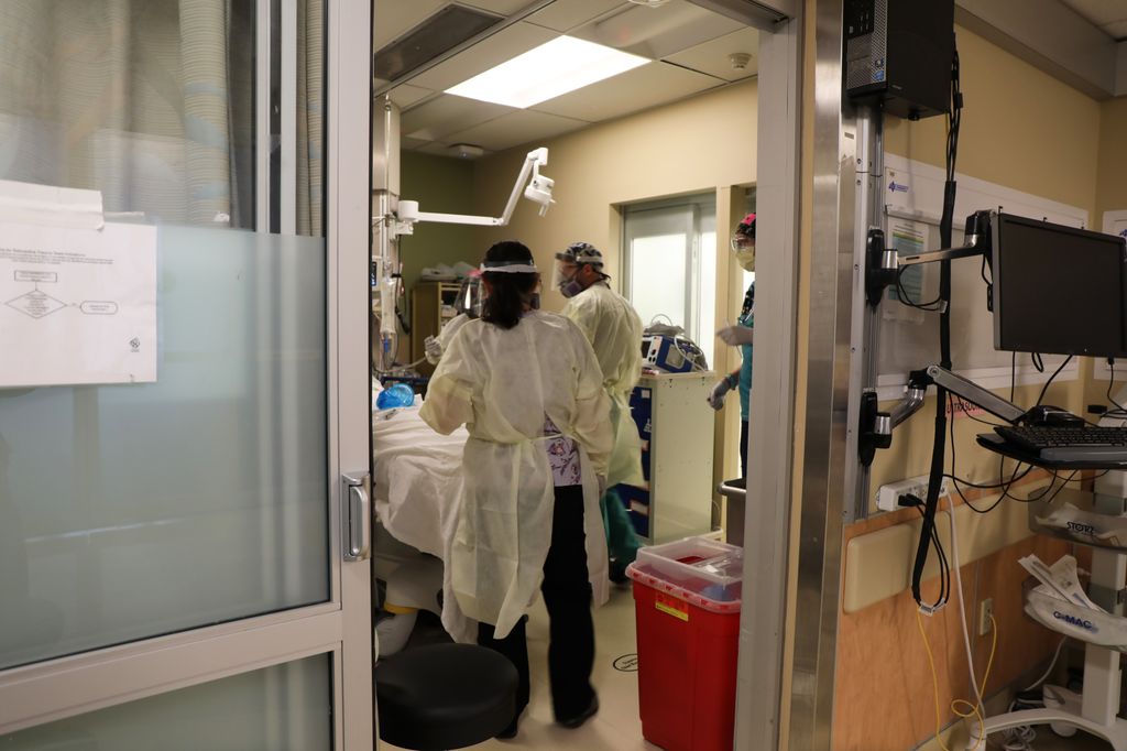OHSU COVID -19 forecast for Feb. 3, 2022. 3 nurses next to a patient bed in emergency room, a female with dark hair, and two men. one tall and one short both with dark hair and all with PPE on.