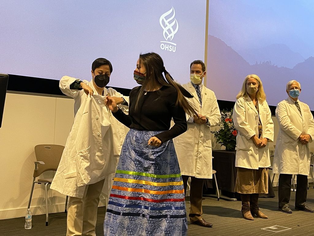 Rebecca Cantone, M.D., assistant dean of student affairs for undergraduate medical education, helps Maliyan Binette, M.D. Class of 2024, don her white coat in the first of the medical school's rites of passage to return in-person since the pandemic began. From left, Benjamin Schneider, M.D., assistant dean for student affairs, Tracy Bumsted, M.D., M.P.H., associate dean for undergraduate medical education, and Interim Dean David Jacoby look on.