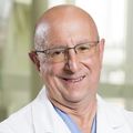 Brett Sheppard, M.D. (OHSU) A person with no hair, in a white coat and glasses, smiling.