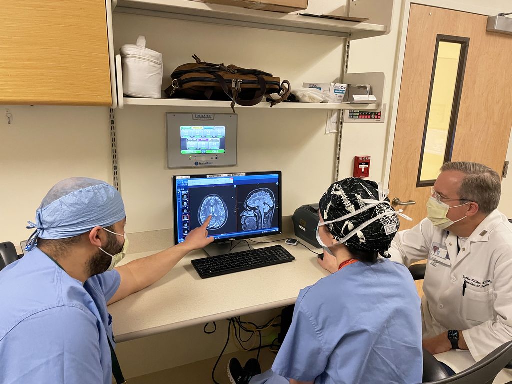 Three neurosurgery professionals looking at a brain scan on a computer and talking about treatment.