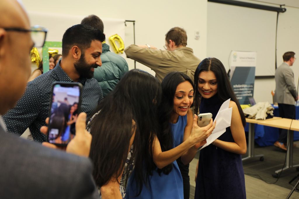 A group of people huddling around a medical graduate with phones out to snap pictures.