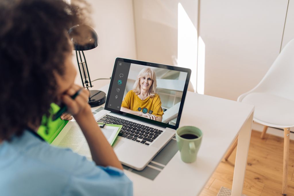 A woman is using her tablet to have a mental health conversation with her patient. Tablet is on a desk in a sunlit room.