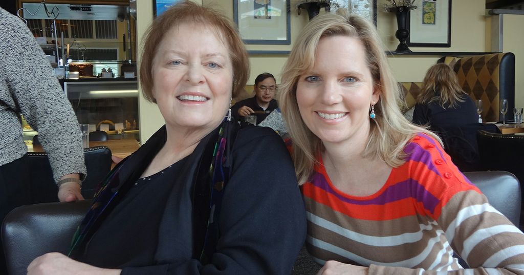 Debi Coleman, left, a woman in a black shirt with brown curly hair, smiling, with her sister, Erin Isselmann, right, in a red and white top at a restaurant for someone's birthday.