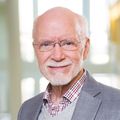 Kent Thornburg, Ph.D. (OHSU) A man with short white hair, in a suit, near a window.