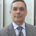 Joaquin E. Cigarroa, M.D. (OHSU) A man with short dark hair in a suit, near a window.