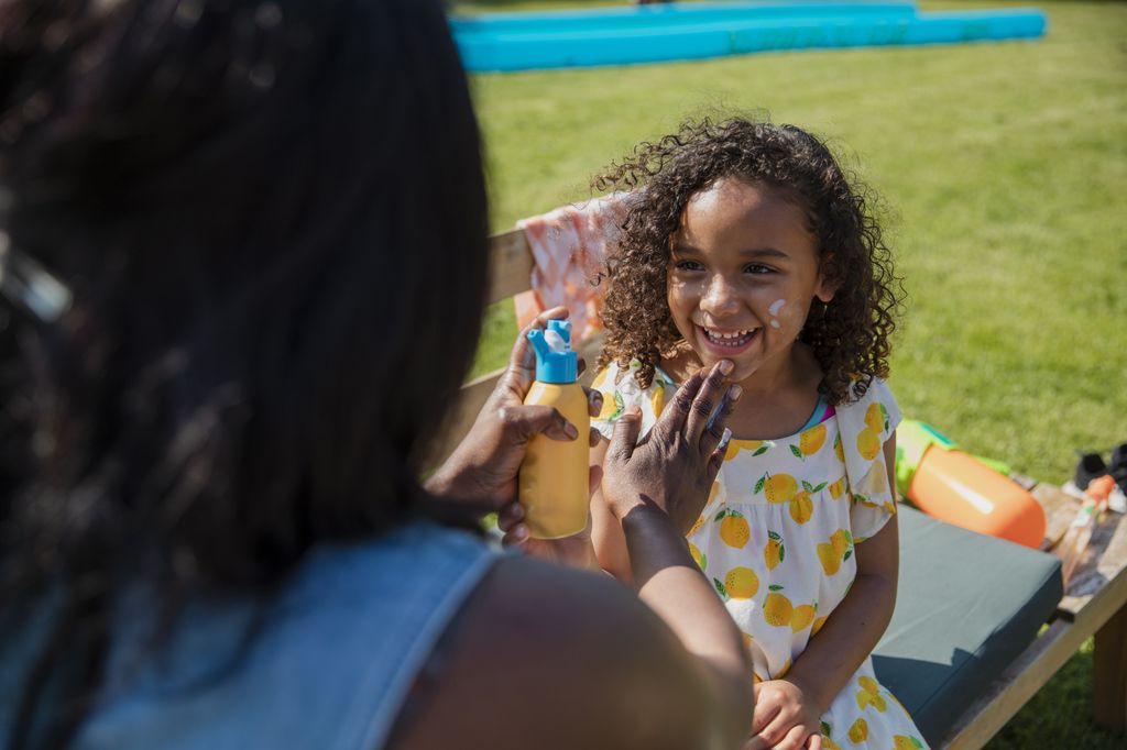 A mom applies sunscreen on her young daughter's face while at a park on a sunny Spring day.