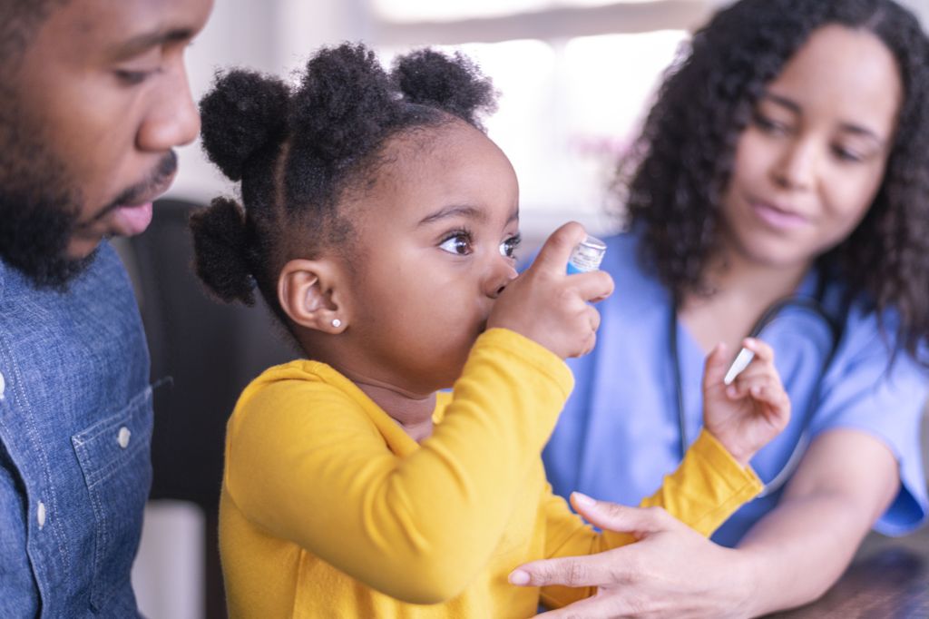 A child demonstrates that she knows how to use an inhaler during her routine asthma checkup. Her father and a nurse look on.&nbsp;Asthma-related emergency department use is highest among people of color, according to a recent study by OHSU researchers. (Getty Images)